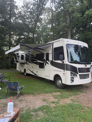 A white RV with a large awning, a dining table with chairs, and a camping chair. - Skip the ordinary hotel—stay somewhere unforgettable. (Leesburg)