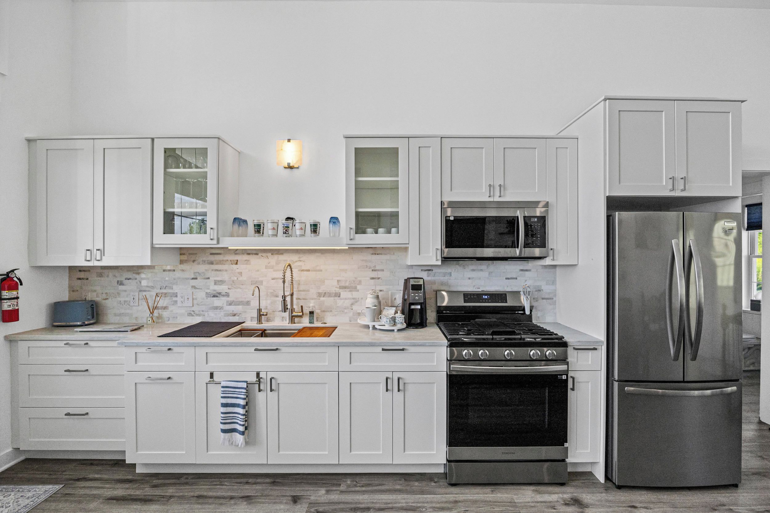 Cocina moderna con armarios blancos, refrigerador de acero inoxidable, microondas integrado y estufa a gas.