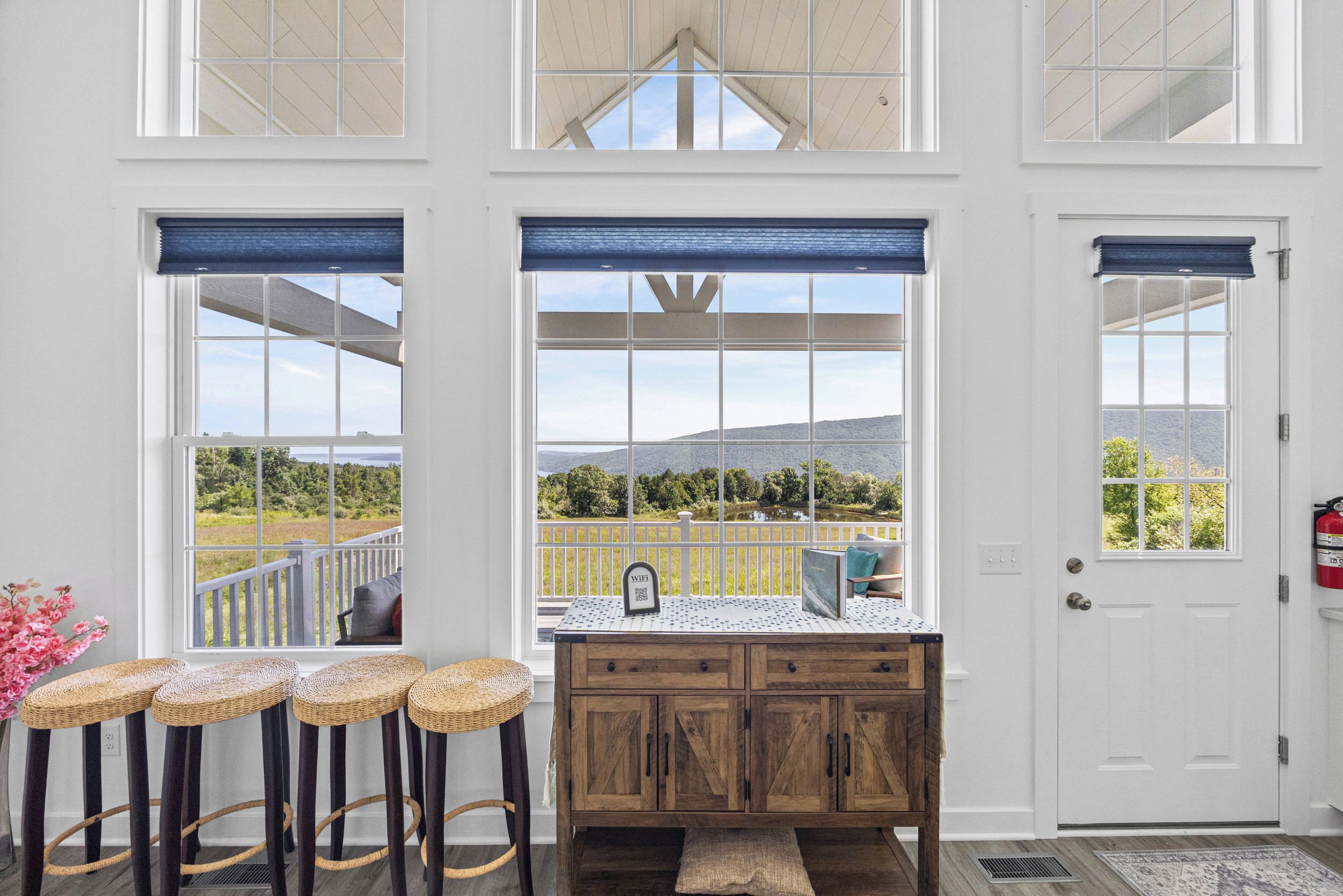 A room with a wooden cabinet, a bench with stools, and a view of a landscape through large windows.