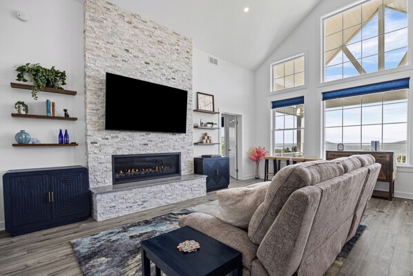 A modern living room with a stone fireplace, a flat-screen TV, and a large window offering a view.