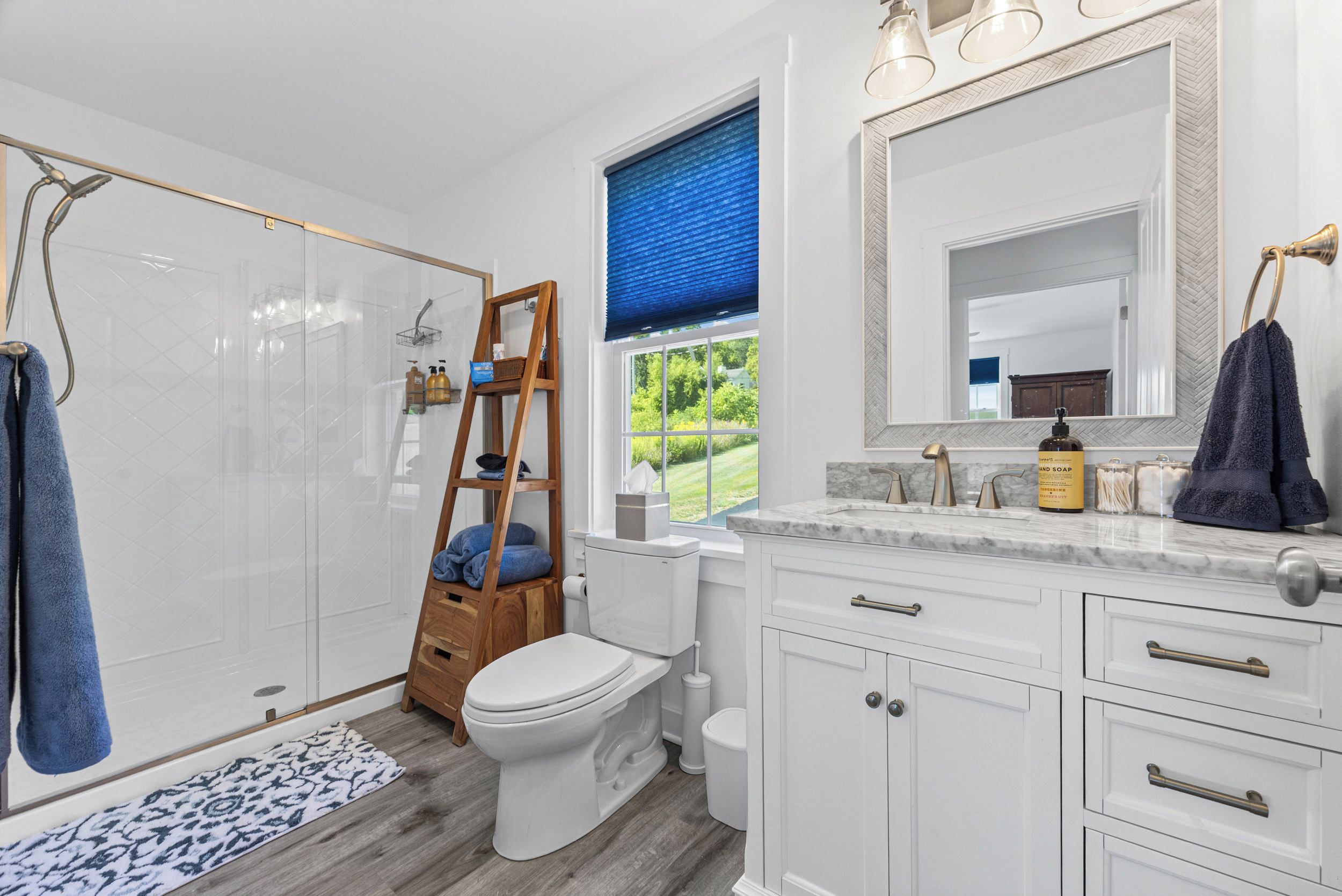 Une salle de bain dotée d’une douche à parois de verre, d’une échelle en bois, de toilettes, d’un lavabo avec un plan de travail en marbre et d’un grand miroir.