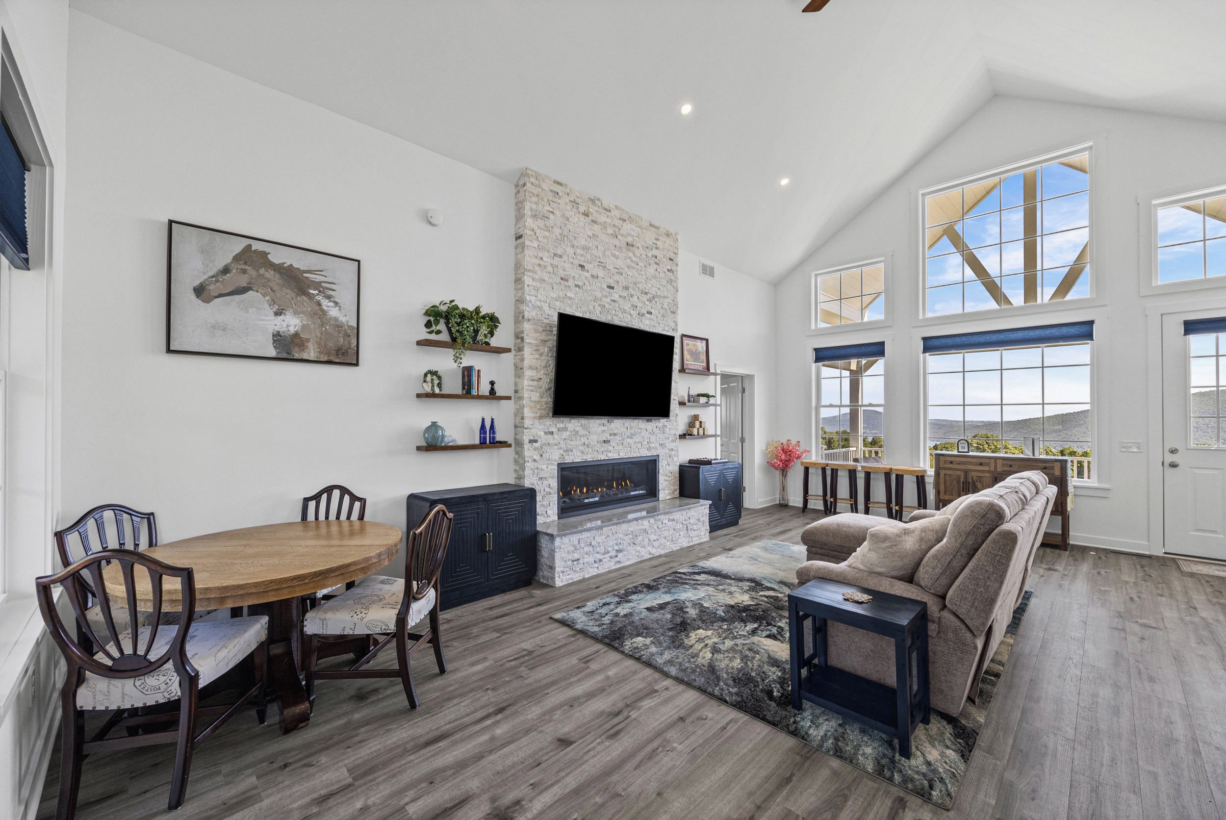 A spacious living area with a fireplace, a dining table with chairs, a sofa, and a large window offering a view of the outdoors.