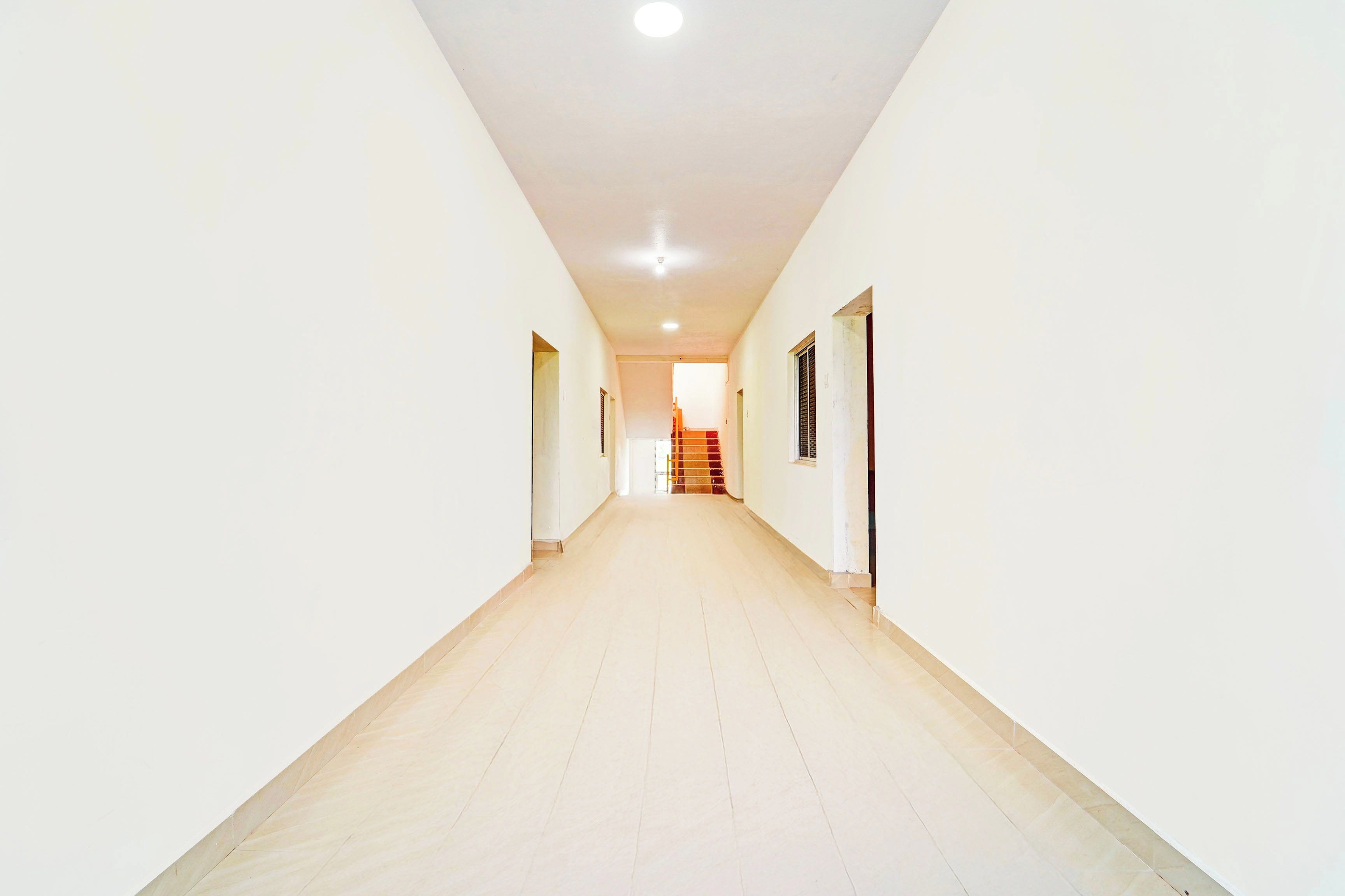 A long, narrow hallway with white walls and a light-colored floor, leading to a staircase.