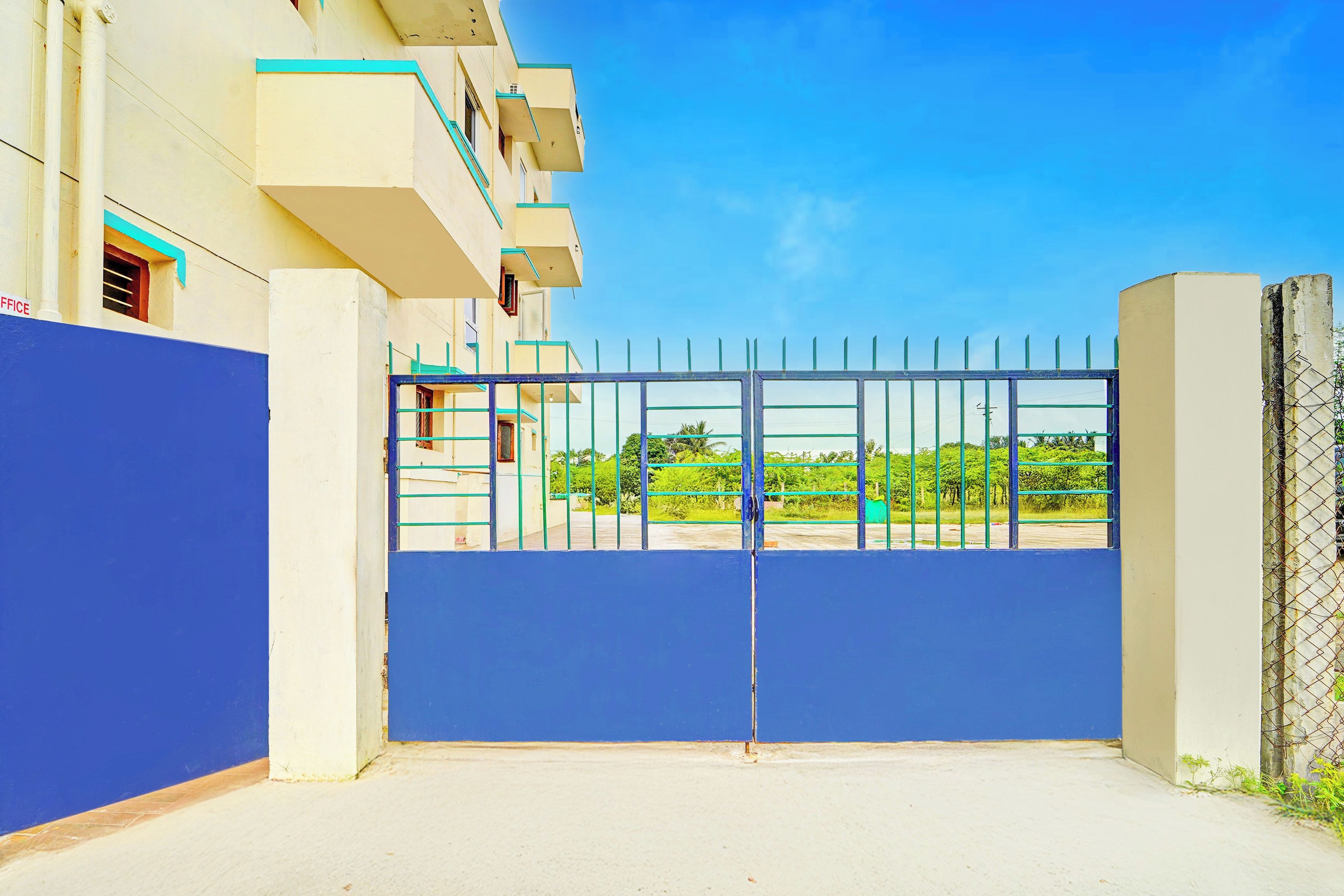 Une entrée fermée par un portail donnant accès à un immeuble avec un mur bleu et un portail en métal.