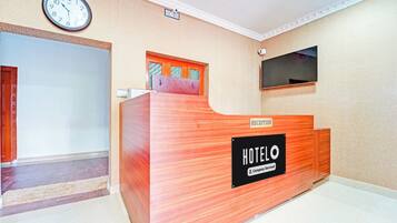 A hotel reception desk with a clock above it, a reception sign, and a television mounted on the wall.