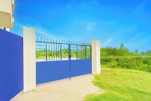 A gated entrance with a blue wall and metal gate, leading to a building with a clear sky in the background.
