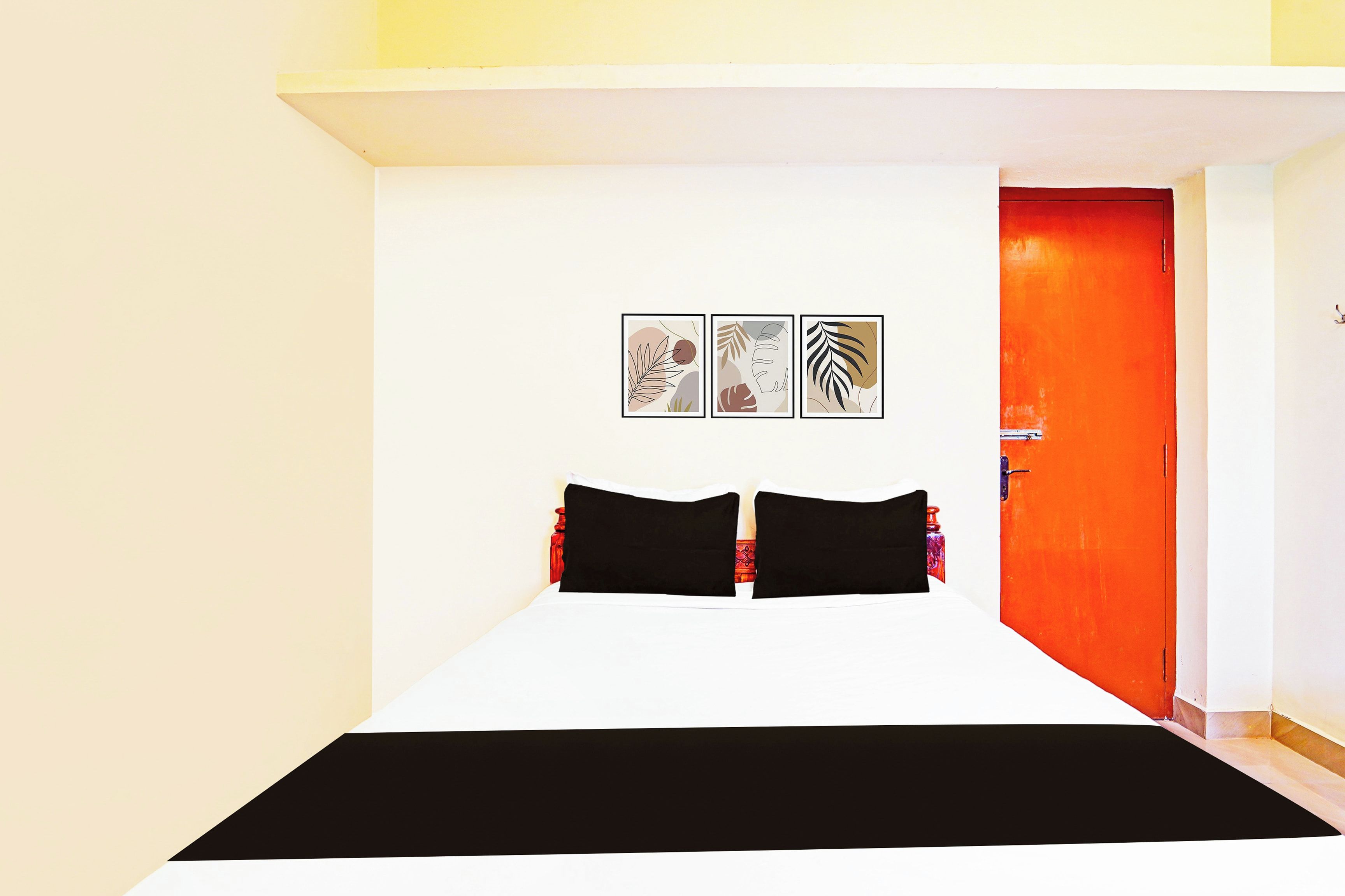 Una habitación con una cama, una puerta roja y tres cuadros en la pared.