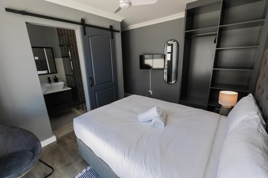 A modern hotel room with a bed, a desk, a chair, a wardrobe, a mirror, and a bathroom.