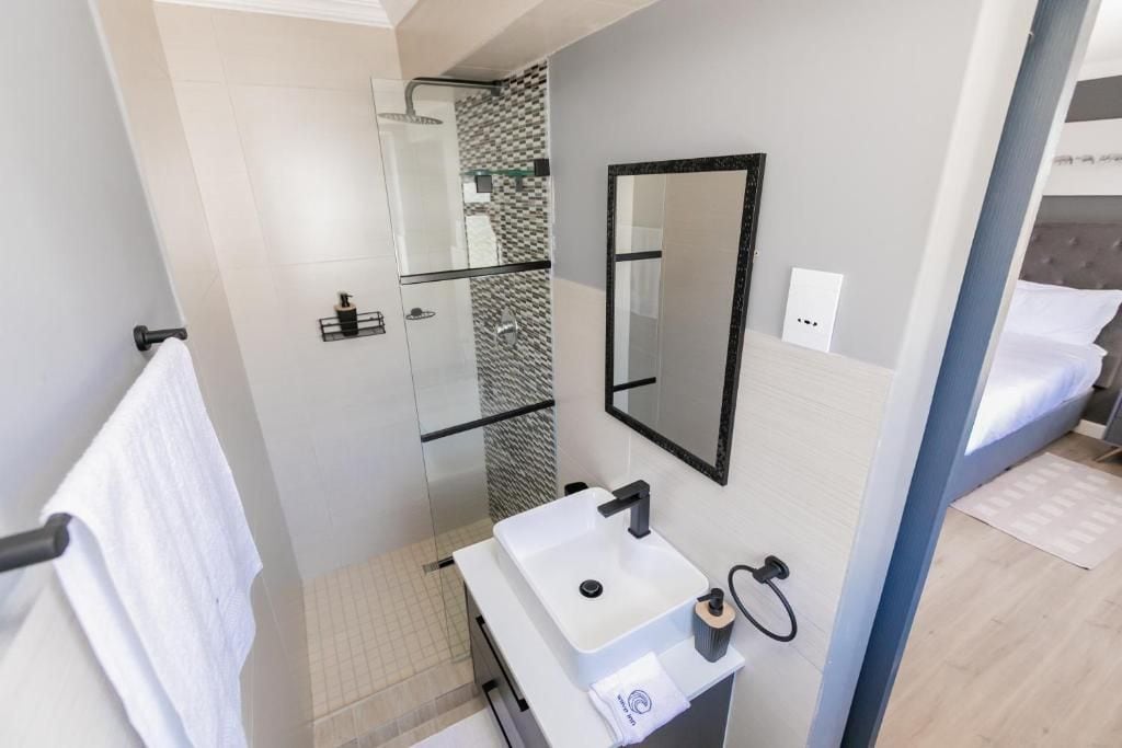 A modern bathroom with a glass shower enclosure, a white sink, and a large mirror.