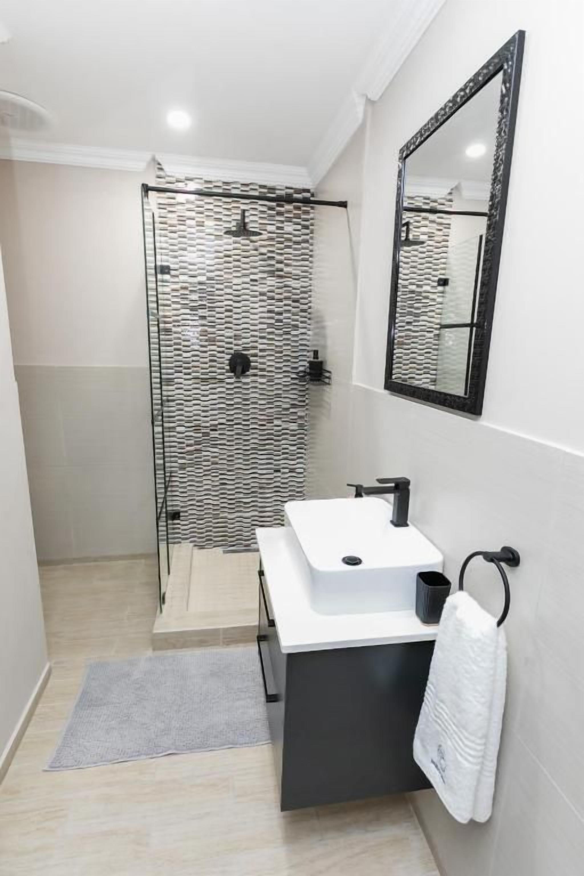 Une salle de bain moderne avec une douche à l’italienne en verre, un lavabo blanc et un meuble noir.