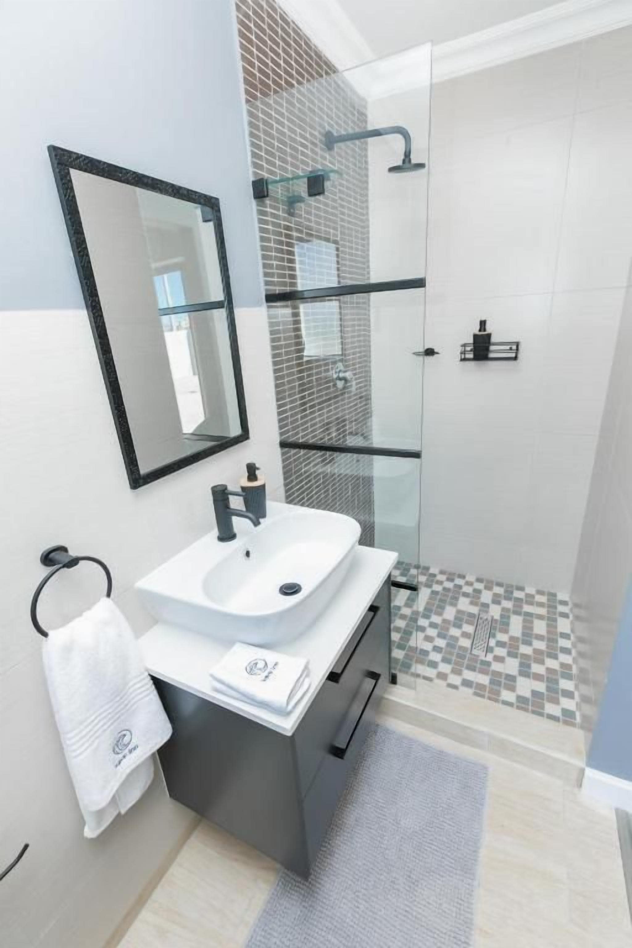 A modern bathroom with a glass-enclosed shower, a white sink, and a mirror.