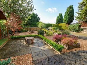 A garden with a paved walkway, a wooden bench, and various plants. - Camusfearna (Castle Douglas)