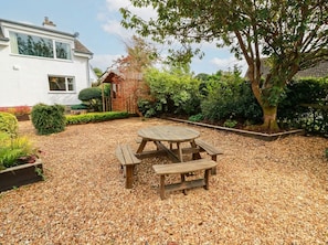 A patio with a wooden table and benches, surrounded by gravel and greenery. - Camusfearna (Castle Douglas)