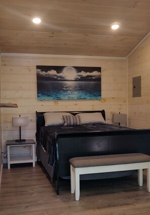 Une chambre à coucher avec un lit, des tables de chevet, un banc et un tableau représentant un ciel nocturne.