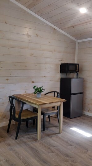 A small kitchen with a wooden table, chairs, a potted plant, a microwave, and a refrigerator. - Hill Top Cabin overlooking The Pond! (Granite Falls)