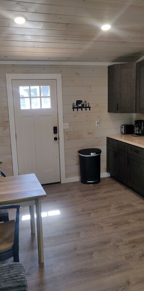 Une cuisine avec des murs en bois, une porte blanche, une poubelle et des meubles de rangement sombres.