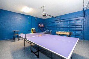 A room with a ping pong table, a foosball table, and a basketball hoop. - Windsor Cay 7BR | Themed rooms, pool & spa (Clermont)