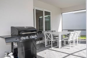 An outdoor patio with a black Char-Broil grill, a white table, and chairs. - Windsor Cay 7BR | Themed rooms, pool & spa (Clermont)