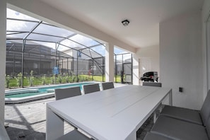 Een overdekt buitengebied met een zwembad, een tafel en stoelen.