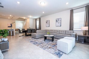 Een moderne woonkamer met een hoekbank, een salontafel en een eetgedeelte met stoelen.