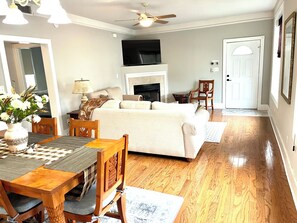 A living room with a sofa, a coffee table, a fireplace, and a dining area with a table and chairs. - Shadow Brooke Village Unit 100 • FLETC & Vacation 3BR Condo w/Garage (St. Simons Island)
