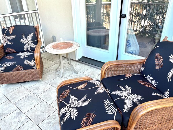 A patio area with wicker furniture and a small round table. - Shadow Brooke Village Unit 100 • FLETC & Vacation 3BR Condo w/Garage (St. Simons Island)