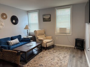 Ein Wohnzimmer mit blauem Sofa, beigem Sessel, Couchtisch aus Holz und einem gemusterten Teppich.