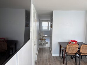 A modern kitchen with white cabinetry, a dining area with wicker chairs, and a view into the dining room. - 2-Bedroom Close to UNH & Portsmouth ~ Parking! (Dover)
