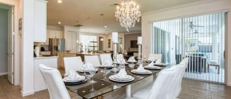 A dining area with a glass table, white chairs, and a chandelier.
