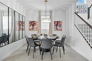 Een eetruimte met een ronde tafel, grijze stoelen en een kroonluchter.