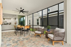 A modern patio area with a dining table and chairs, a ceiling fan, and wicker furniture. - 7BR Solara | Themed rooms, cinema, pool & spa (Kissimmee)