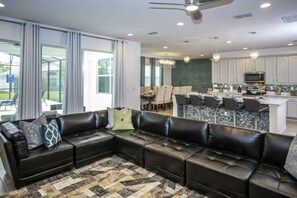 A modern living room with a sectional sofa, dining area, and kitchen. - 7BR Kissimmee home | Pool, cinema, games (Kissimmee)