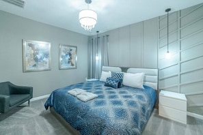 A modern bedroom with a large bed, a bedside table, a chair, and two wall-mounted artworks. - 8BR themed home near Disney | Pool & game room (Kissimmee)
