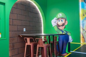 A room with a green wall, a brick archway, a Mario character mural, and a table with chairs. - 9BR Solara home | Pool, spa & themed rooms (Kissimmee)