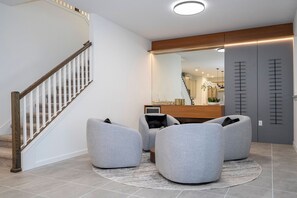 A modern interior with a staircase, grey upholstered chairs, a wooden cabinet, and a mirror. - 9BR Solara home | Pool, spa & themed rooms (Kissimmee)