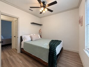 Ein Schlafzimmer mit einem Bett, einem Deckenventilator, einem Fenster mit Jalousien und einer Tür zu einem anderen Raum.