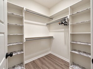 Un vestidor con paredes blancas, estantes con diseño de mármol y suelo de madera.