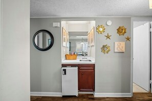 A kitchen with a refrigerator, a sink, and a mirror. There are decorative wall hangings and a door with a handle. - Pelicans Watch 204- 3BR Steps From The Beach (Myrtle Beach)