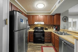 A compact kitchen with a refrigerator, stove, sink, and wooden cabinets. - Pelicans Watch 204- 3BR Steps From The Beach (Myrtle Beach)