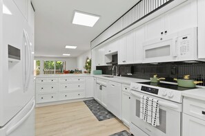 Une cuisine moderne avec des meubles blancs, un four encastré, un four à micro-ondes et une cuisinière.