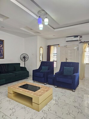 A living room with a sofa, two armchairs, a coffee table, a ceiling fan, and a door with a window. - Spacious 2-Bedroom Escape | Stylish, Serene & Fully Equipped (Agege)