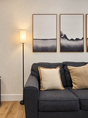 A modern living room with a grey sofa, two framed artworks, a floor lamp, and a textured throw pillow. - King Beds  Tampa Nature Hideaway Chic 2BR (Tampa)