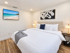 Ein Hotelzimmer mit Bett, Nachttisch, Wandfernseher und Kunstwerken.