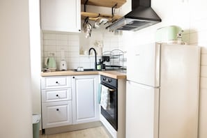A kitchen with white cabinets, a black oven, a green kettle, and a white refrigerator. - Studio apartment Milica in the stone house near the beach (Kaštel Novi)