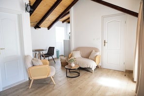 Una habitación con techo de madera, un sofá, una silla, una mesita con un florero y una puerta.