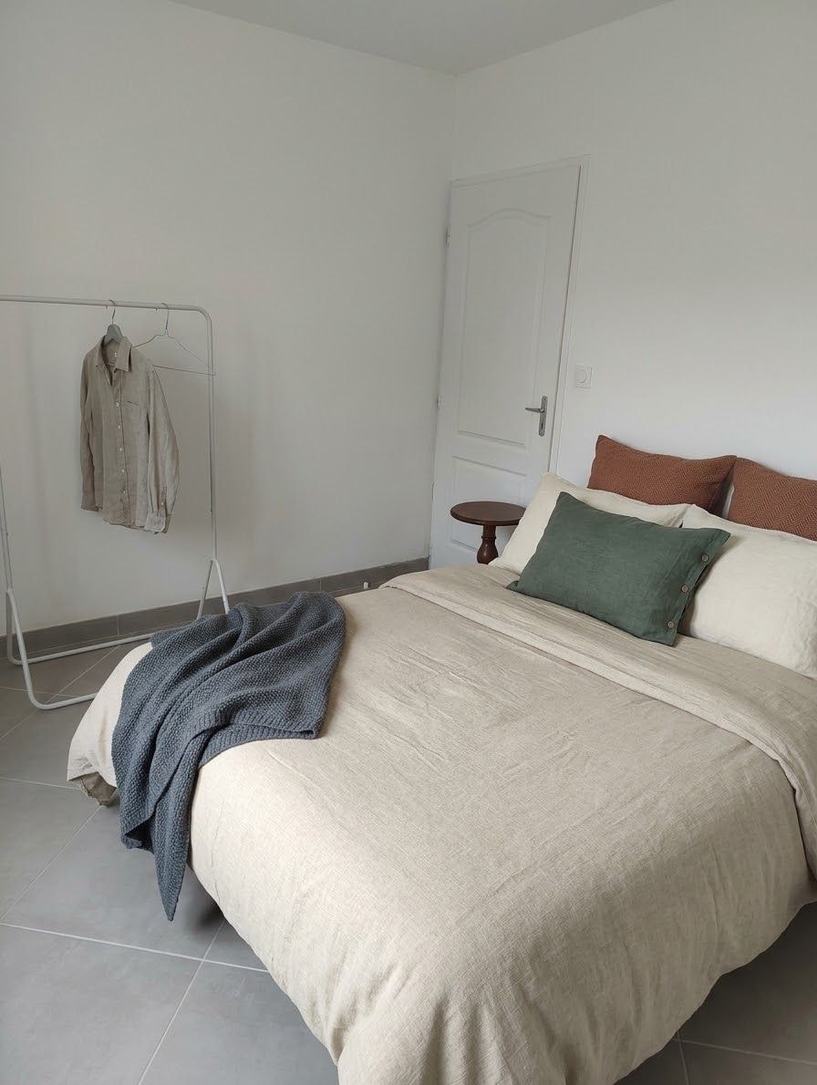 Een slaapkamer met een bed, een kledingrek, een deur en een klein, rond tafeltje.