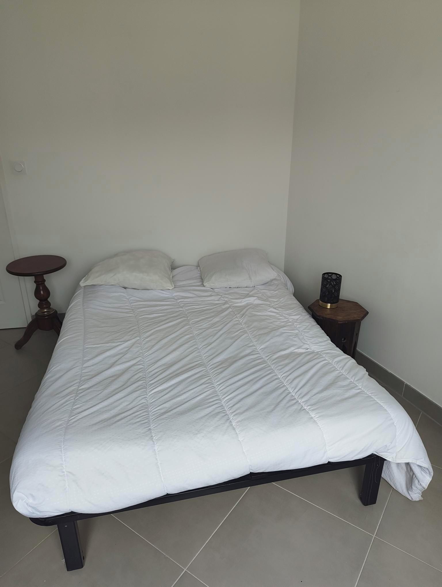 Un lit recouvert d’une couette blanche, une table de chevet en bois avec une lampe et une petite table ronde.