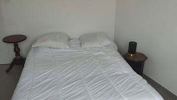 Un lit recouvert d’une couette blanche, une table de chevet en bois avec une lampe et une petite table ronde.