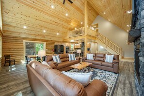 Ein geräumiges Wohnzimmer mit hoher Decke und Holzbalken, einer Wand aus Naturstein und einer gemütlichen Sitzecke mit Ledersofas und einem Couchtisch.