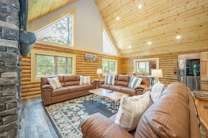 L’intérieur d’une cabane en rondins, avec un grand canapé en cuir marron, une table basse et une cheminée.